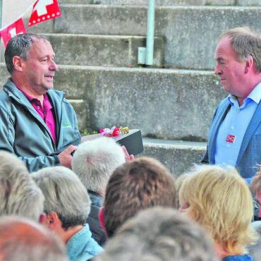 Von Schminke und der Liebe - Vizeammann Peter Brütsch überreicht dem Gastredner Alois Huber (links) ein Geschenk – die Bevölkerung spendet Applaus. Bild: Annemarie Keusch